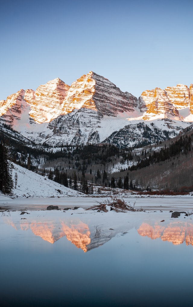 Snow-capped mountain peaks reflected in a calm alpine lake, showcasing mountain travel destinations.